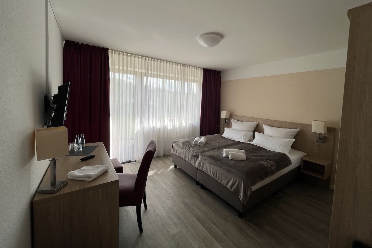 A hotel room with a bed, desk, chair, and curtains.