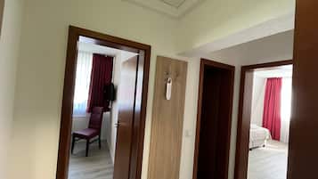 Un pasillo de hotel con puertas de madera que dan a una habitación con cama y otra habitación separada con una silla y un altavoz.