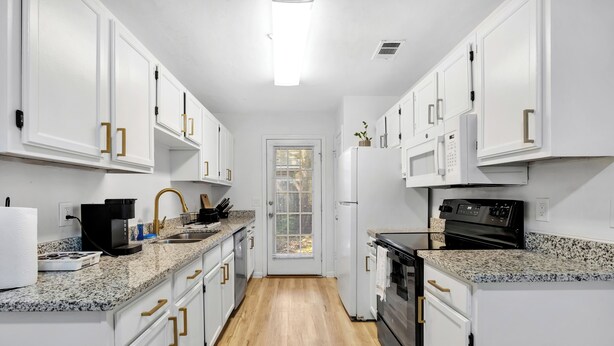 A narrow kitchen with white cabinets, granite countertops, and a black stove. - Contemporary and Lux Townhome - 5 mins to FSU (Tallahassee)