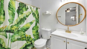 A bathroom with a toilet, a sink with a gold faucet, a mirror with a gold frame, and a shower curtain with a leaf pattern. - Contemporary and Lux Townhome - 5 mins to FSU (Tallahassee)