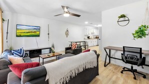 A modern living room with a sofa, coffee table, and a desk with a chair. A ceiling fan and a TV are mounted on the wall. - Contemporary and Lux Townhome - 5 mins to FSU (Tallahassee)