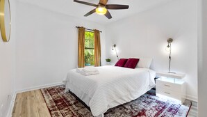 A bedroom with a bed, a ceiling fan, a nightstand with a lamp, and a window with curtains. - Contemporary and Lux Townhome - 5 mins to FSU (Tallahassee)