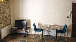 Una habitación con pared de piedra, un televisor sobre un pedestal de madera, una mesa redonda con dos sillas y un techo de madera con vigas a la vista.