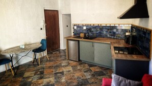 Una cocina compacta con salpicadero de azulejos, armarios de madera, un refrigerador pequeño y una zona de comedor con una mesa y sillas.