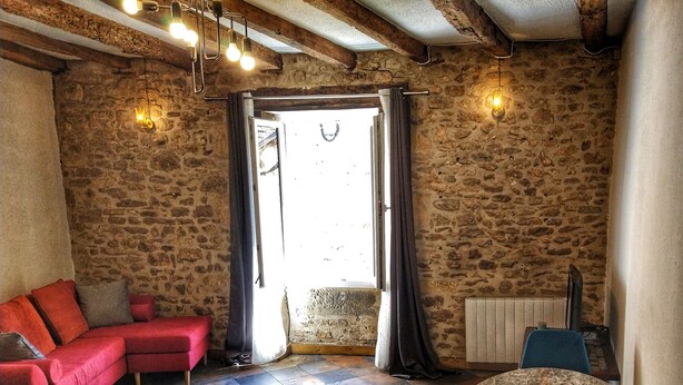 Una habitación acogedora con pared de piedra, un sofá rojo, una mesa redonda con velas y un banco de madera.