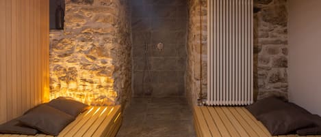 A spa room with stone walls, a wooden bench, and a shower area.