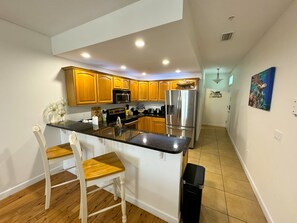 A modern kitchen with wooden cabinets, stainless steel appliances, and a black countertop. - Blue Crab Condo at Rivers Edge (Steinhatchee)