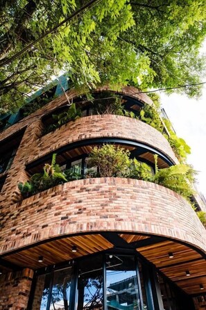 A multi-story building with brick walls and wooden beams, featuring balconies with greenery. - Nomada Hotel Origen (Medellín)