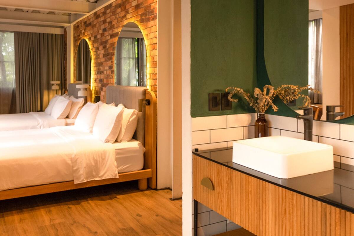 A bedroom with a brick wall, a wooden bed, and a green accent wall in the bathroom with a white sink and mirror.