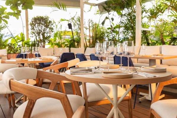 An outdoor dining area with round tables and chairs, surrounded by lush greenery. - Nomada Hotel Origen (Medellín)