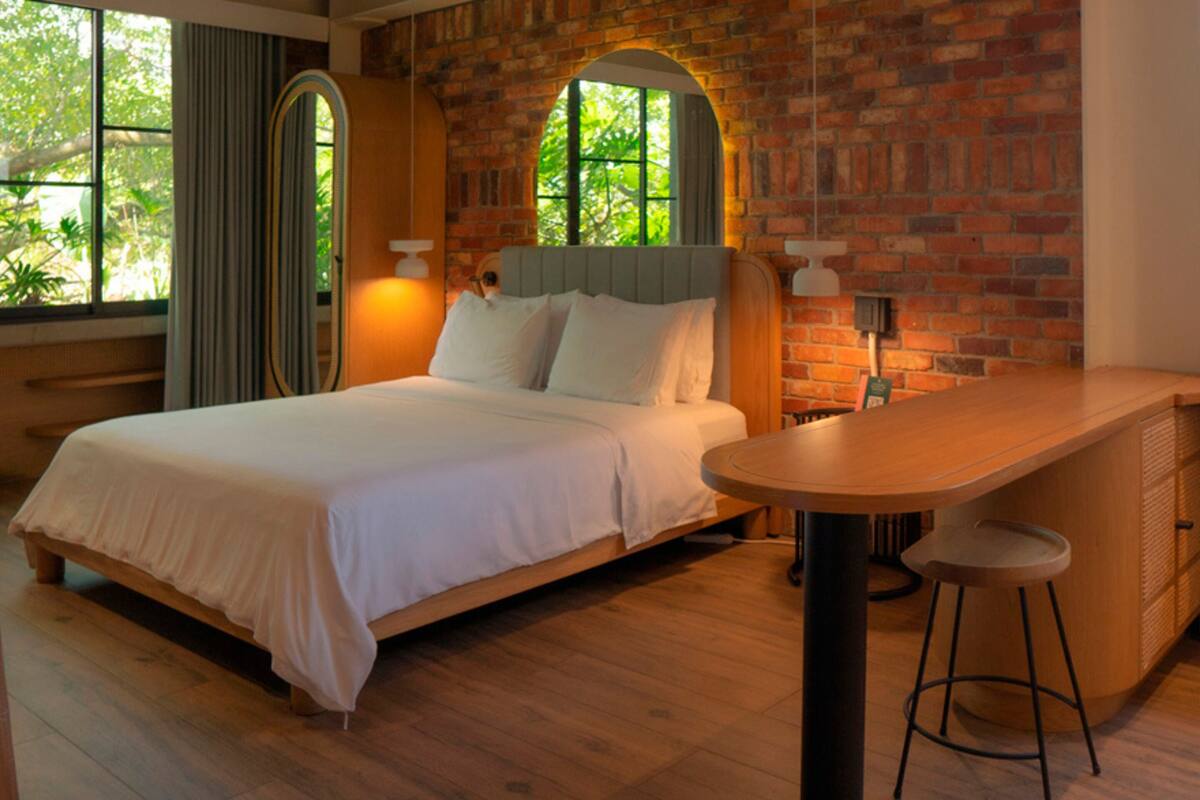 A modern bedroom with a large bed, a wooden desk, and a brick wall.