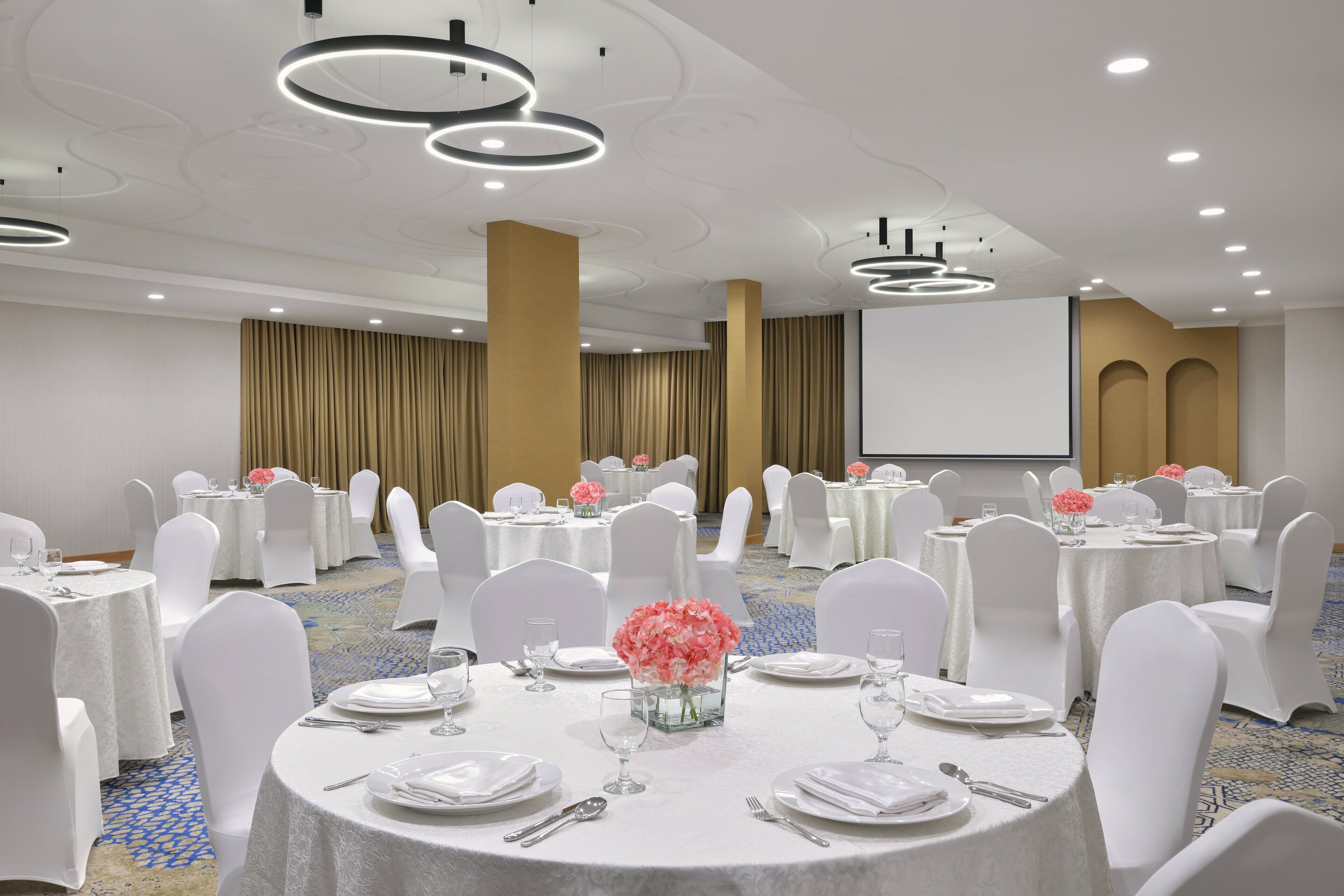 A banquet hall with round tables, white chairs, and floral centerpieces.