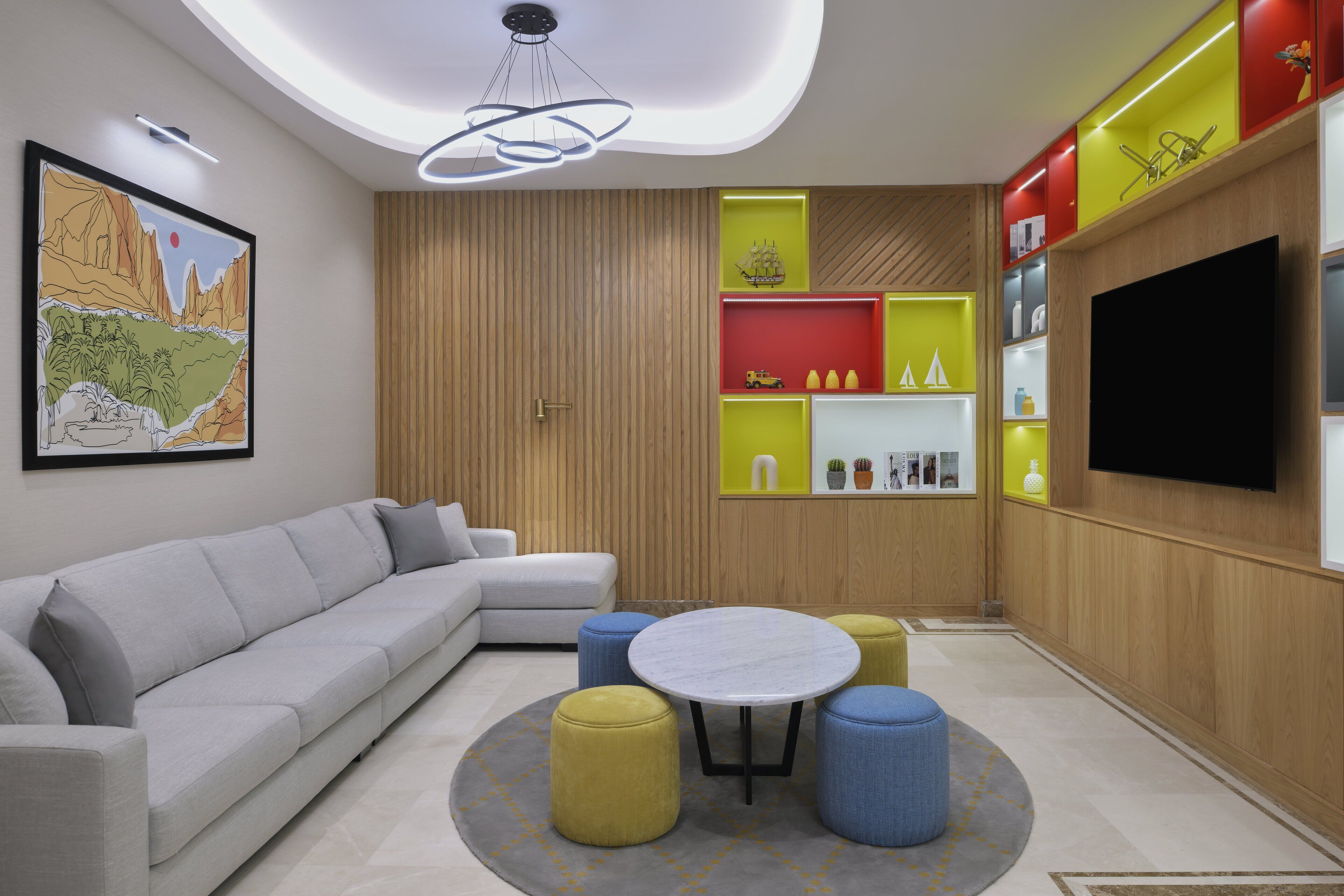 Een moderne woonkamer met een grijze bank, een ronde tafel en kleurrijke poufs.