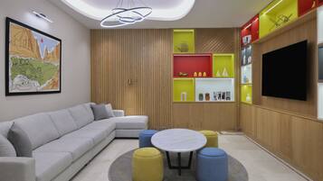 A modern living room with a grey sofa, a round table, and colorful ottomans.