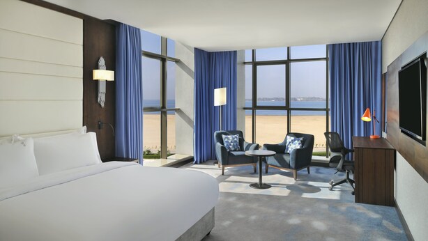 Ein Hotelzimmer mit einem großen Bett, einem Schreibtisch mit Stuhl, einem kleinen Tisch und einem Fernseher.
