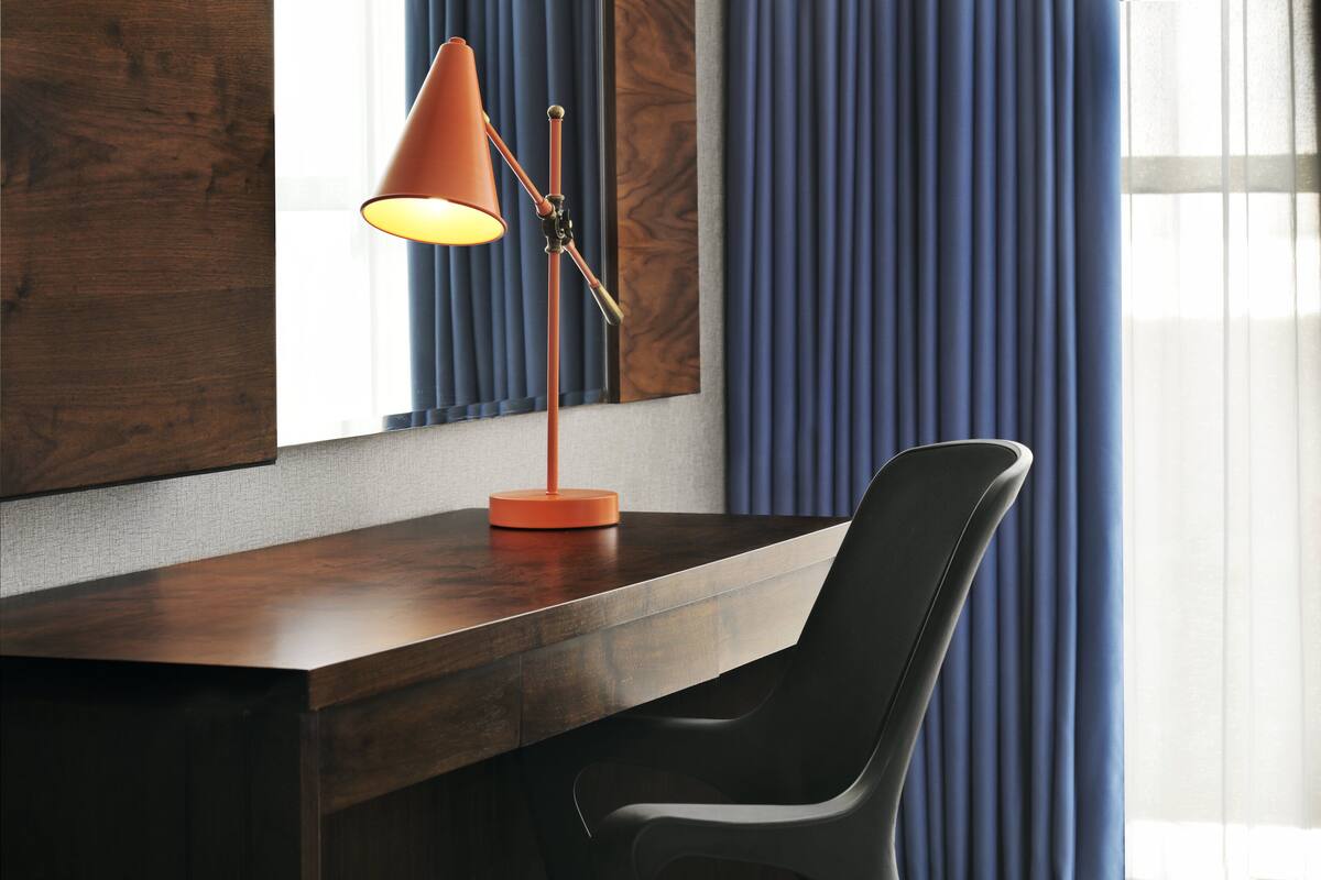 A modern desk with a dark wood finish, a black chair, and an orange floor lamp.