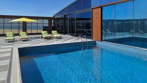 Ein moderner Poolbereich mit Schachbrettmuster-Boden, einem Pool und grünen Liegestühlen.