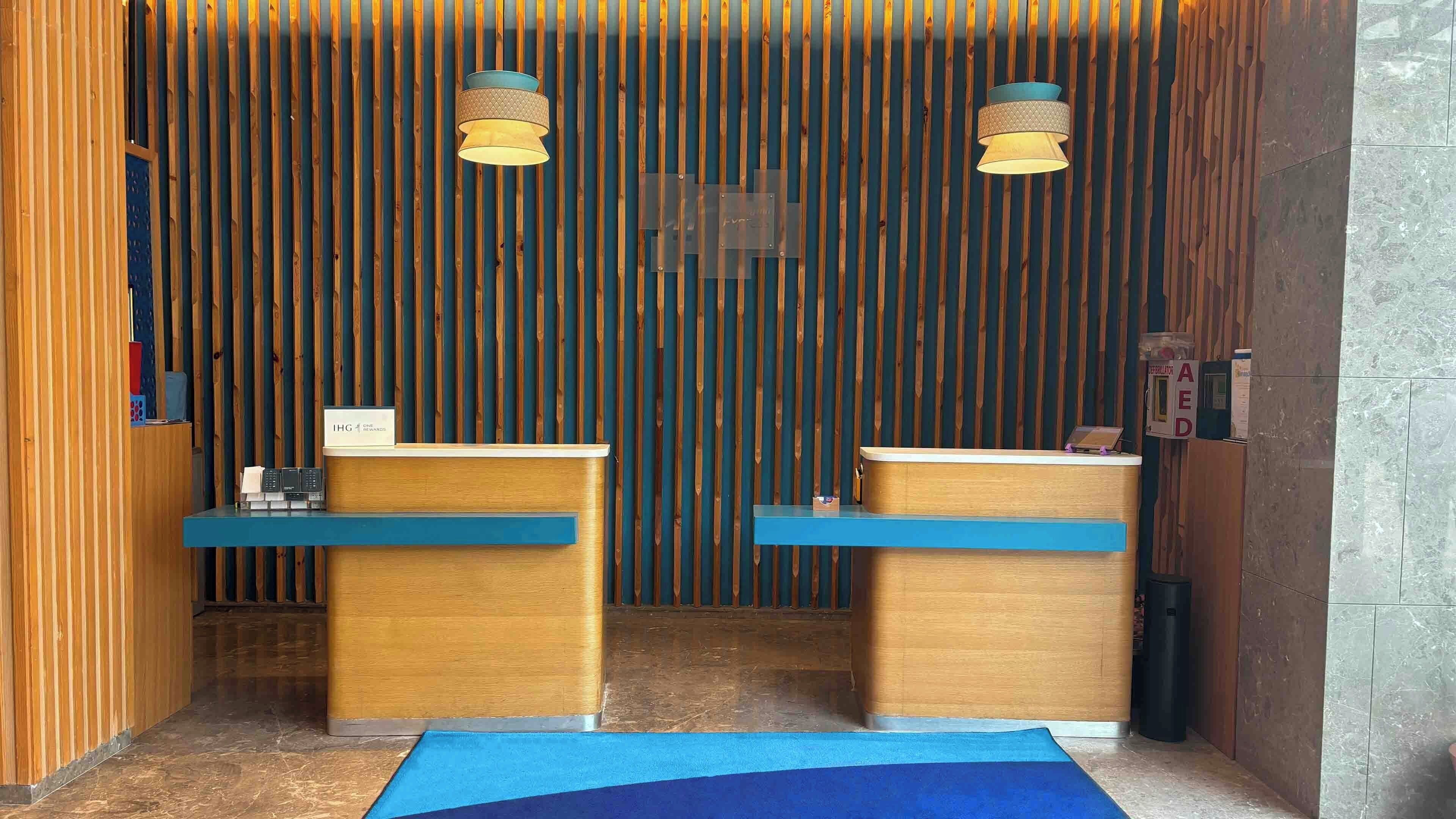 A reception area with two wooden reception desks, a blue carpet, and vertical wooden slats in the background.