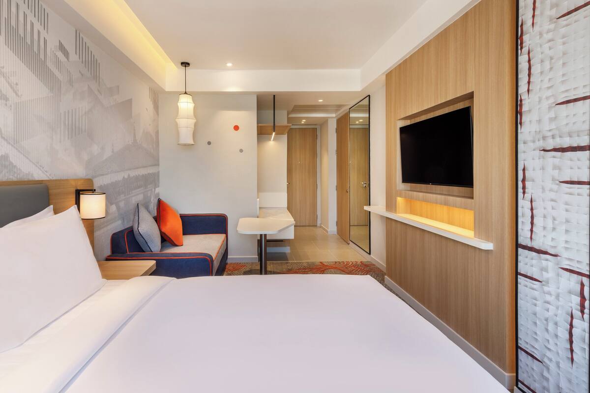 A hotel room with a large bed, a seating area with a table, a TV mounted on the wall, and a mirror.