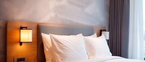 A hotel room with a neatly made bed, a bedside telephone, and a wall-mounted lamp.