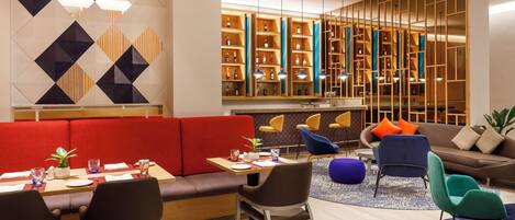 A modern hotel lobby with a red booth seating area, a bar with wooden shelves, and a variety of seating options including chairs and sofas.
