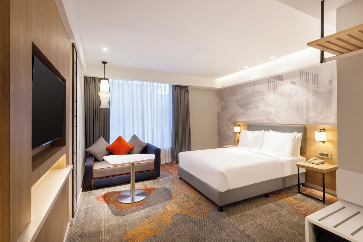 A hotel room with a bed, a sofa, a TV, and a desk with a lamp.