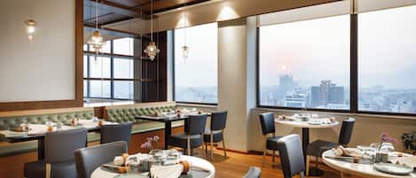 A modern restaurant with high ceilings, large windows, and a city view.