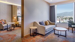 A modern hotel room with a sofa, two side tables, a chair, and a large window offering a city view. - Holiday Inn Express Kathmandu Naxal by IHG (Kathmandu)