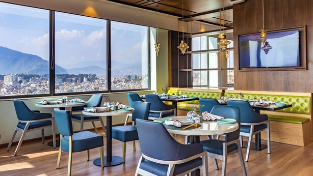 A modern dining area with round tables, blue chairs, and a city view through large windows. - Holiday Inn Express Kathmandu Naxal by IHG (Kathmandu)