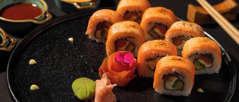 A plate of sushi rolls with dipping sauces and chopsticks on a dark plate.