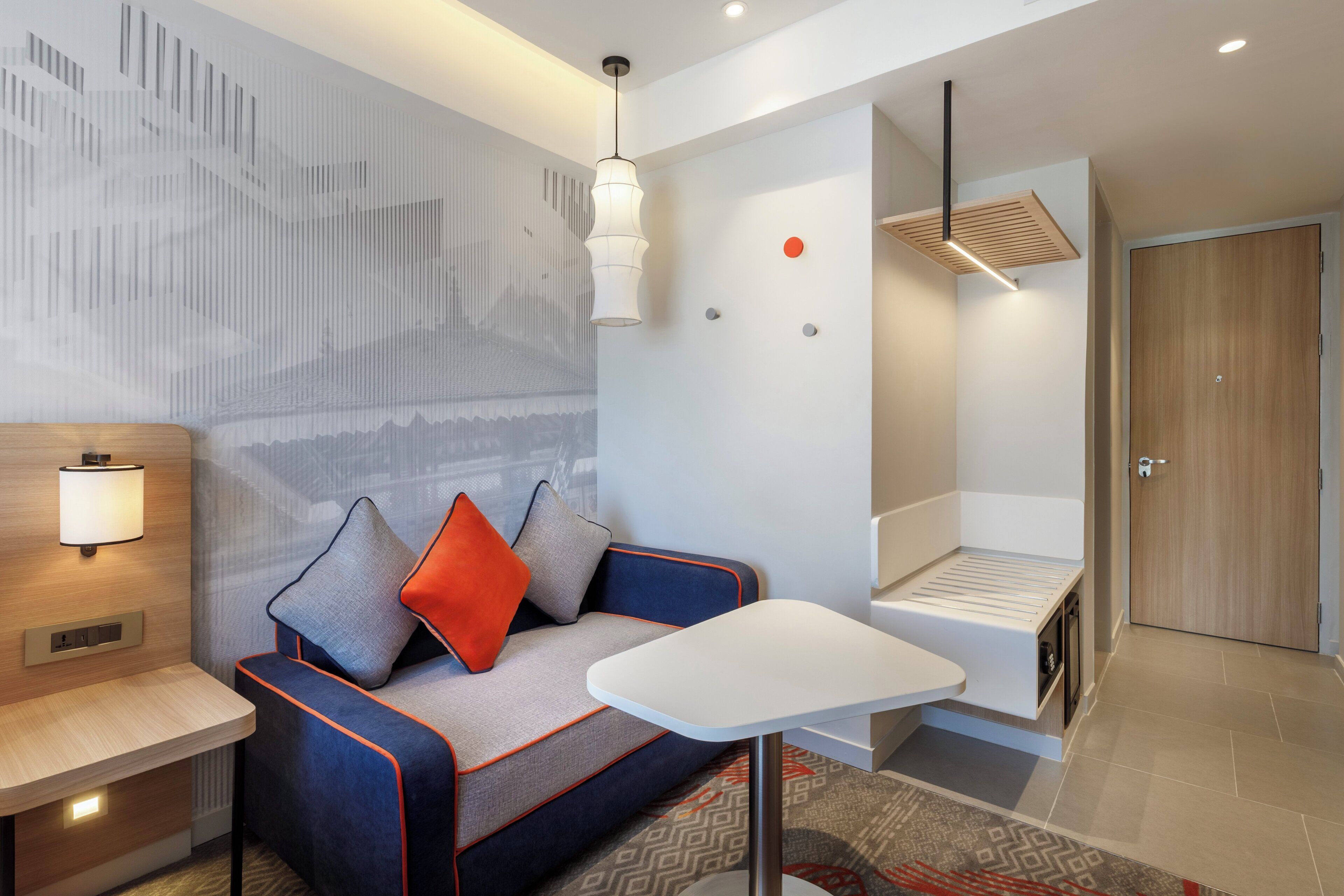 Una habitación de hotel moderna con un sofá, una mesita, una lámpara de pared, una luz en el techo y una puerta.