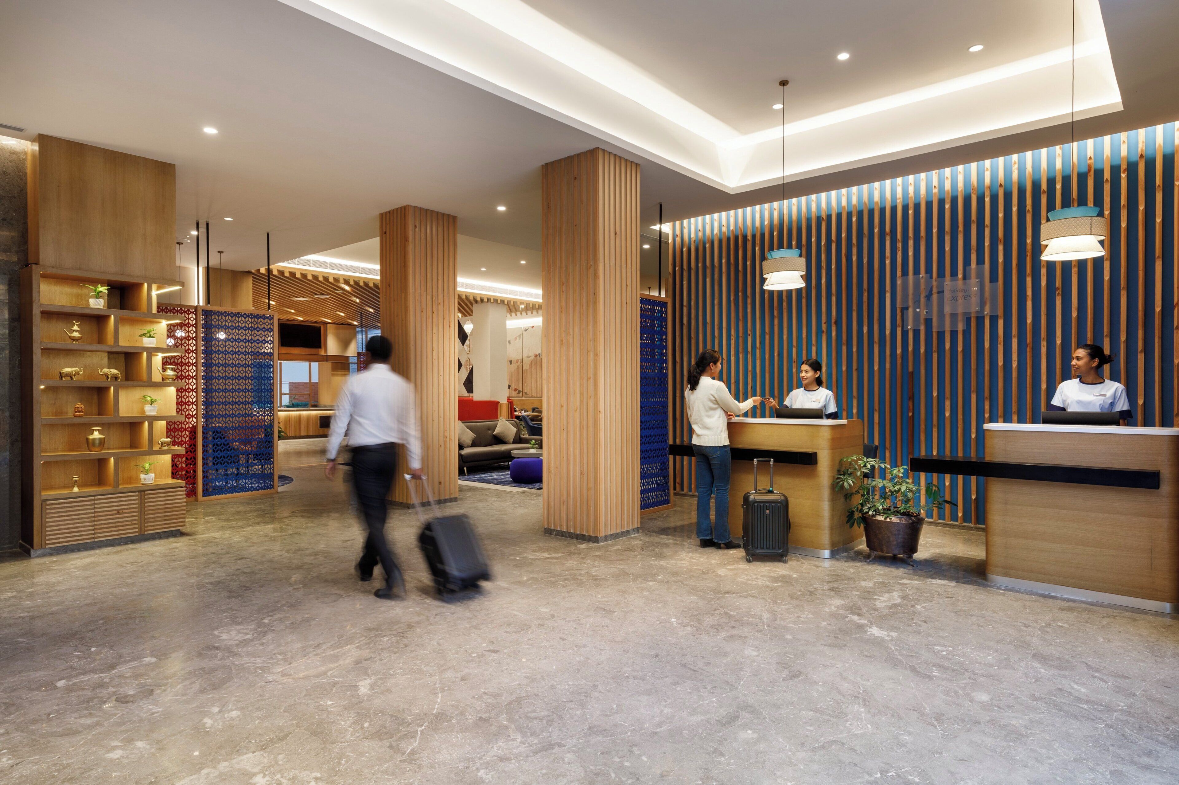 Un moderno vestíbulo de hotel con mostradores de recepción de madera, un área de descanso y un mostrador con una planta.