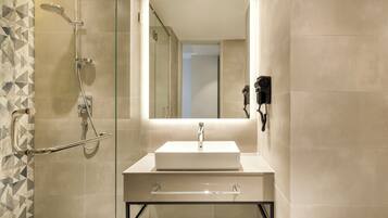 A modern bathroom with a glass shower enclosure, a white sink, and a mirror with a light.