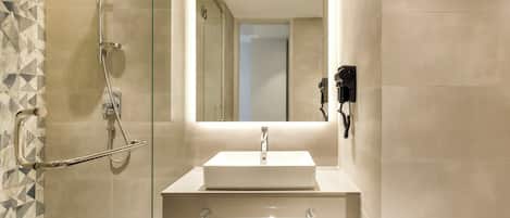 A modern bathroom with a glass shower enclosure, a white sink, and a mirror with a light.