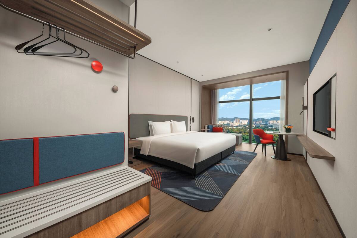 Habitación de hotel moderna con una cama grande, un escritorio y vistas a la ciudad.