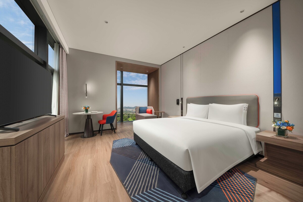 A modern hotel room with a large bed, a desk, and a view of the outdoors.