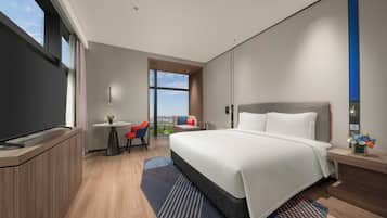 A modern hotel room with a large bed, a desk, a chair, and a view of the cityscape.