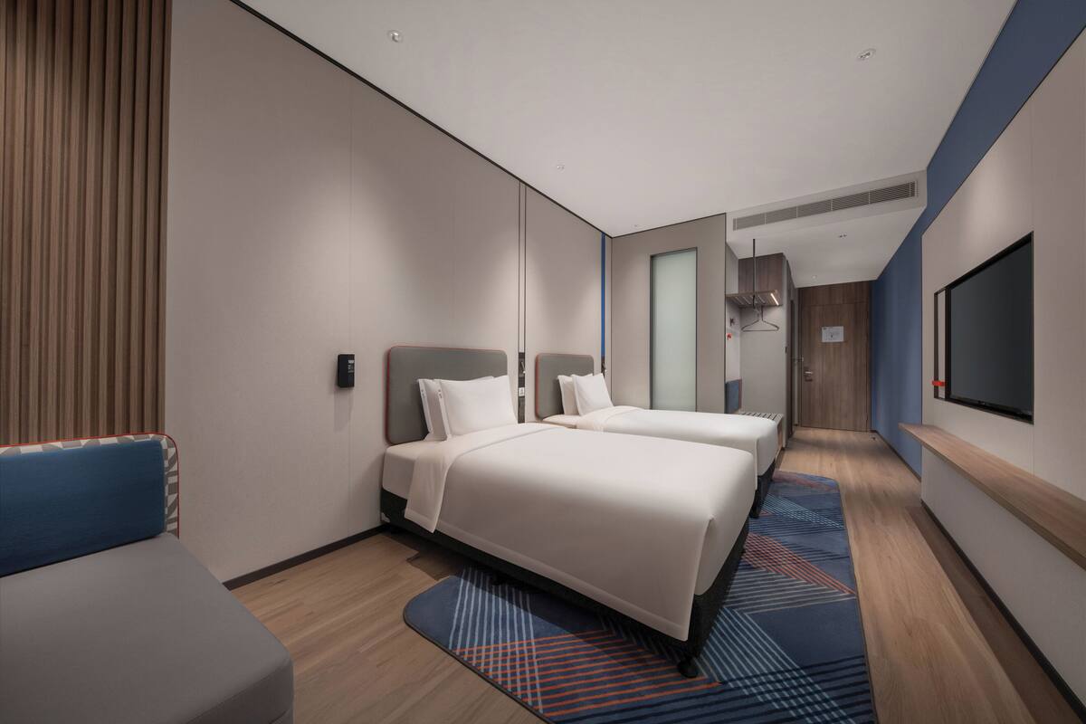 Una habitación de hotel moderna con dos camas, un rincón de descanso, televisión y baño.