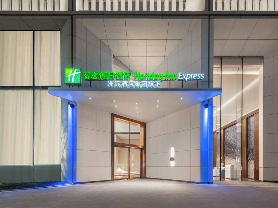 Una entrada de hotel con diseño moderno, con fachada de vidrio y un letrero que indica que pertenece a la cadena Holiday Inn Express.