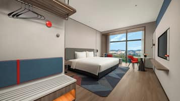 A modern hotel room with a large bed, a seating area, a desk, and a view of the city.
