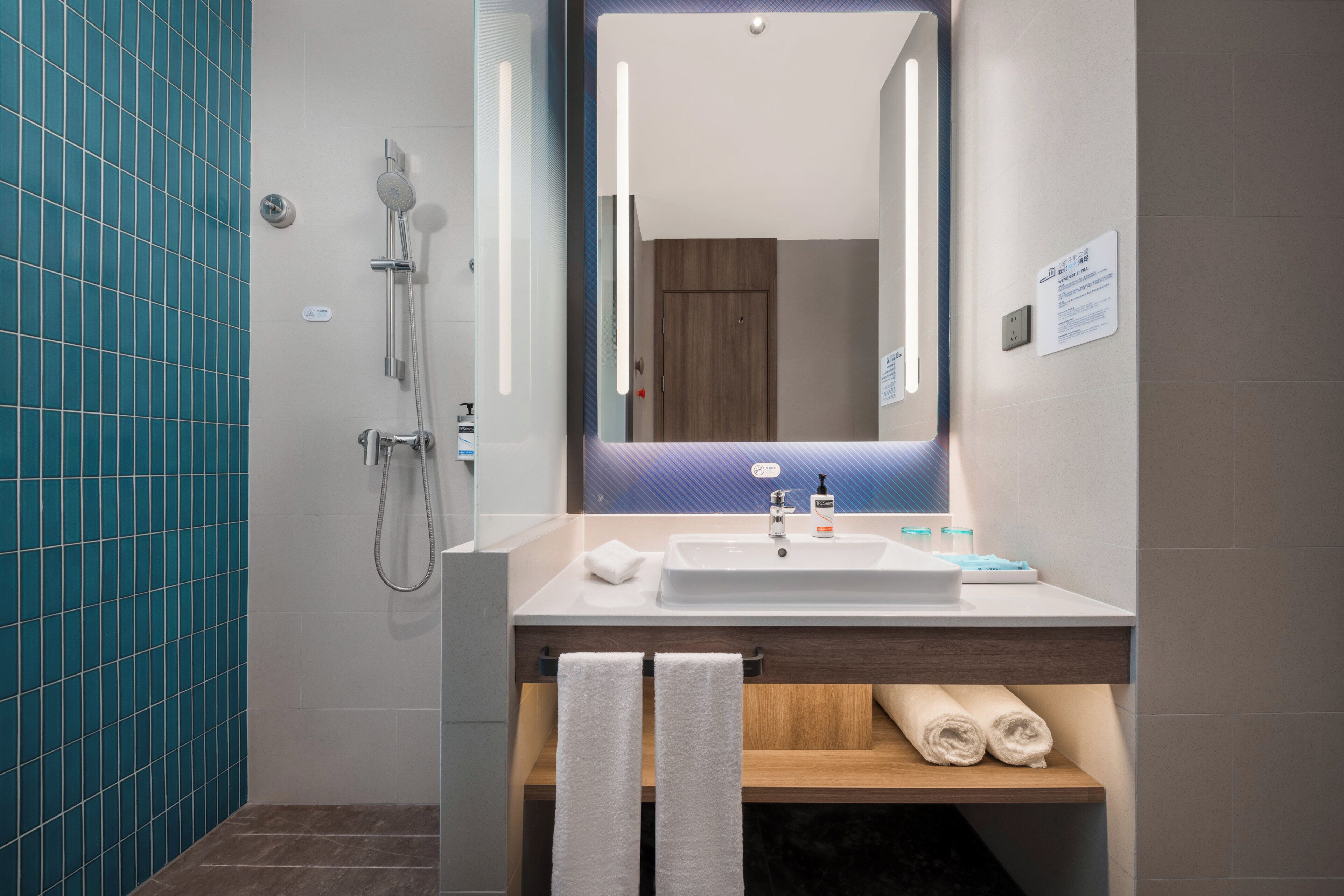 Un bany modern amb un mirall gran, una dutxa i un lavabo amb penjador de tovalloles.