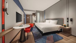 A modern hotel room with a large bed, a desk with a chair, a flat-screen TV, and a small table with a vase of flowers. - Holiday Inn Express Shenzhen Futian Center by IHG (Shenzhen)