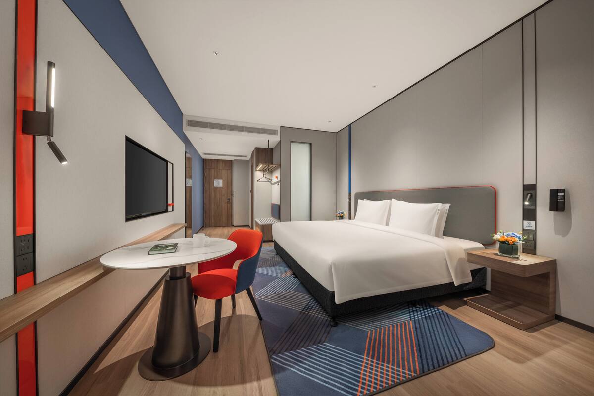 Una habitación de hotel moderna con una cama grande, un escritorio con una silla, un televisor de pantalla plana y una pequeña mesa con un florero.