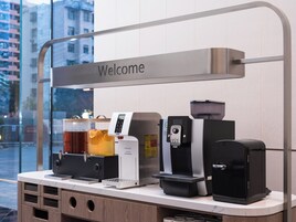 Ein Kaffee-Bereich mit einem ‚Welcome‘-Schild, einem Warmwassergerät, einer Kaffeemaschine und einem Mülleimer.