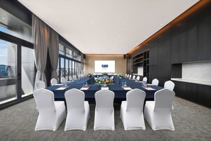 A conference room with a long table, white chairs, and a projector screen.