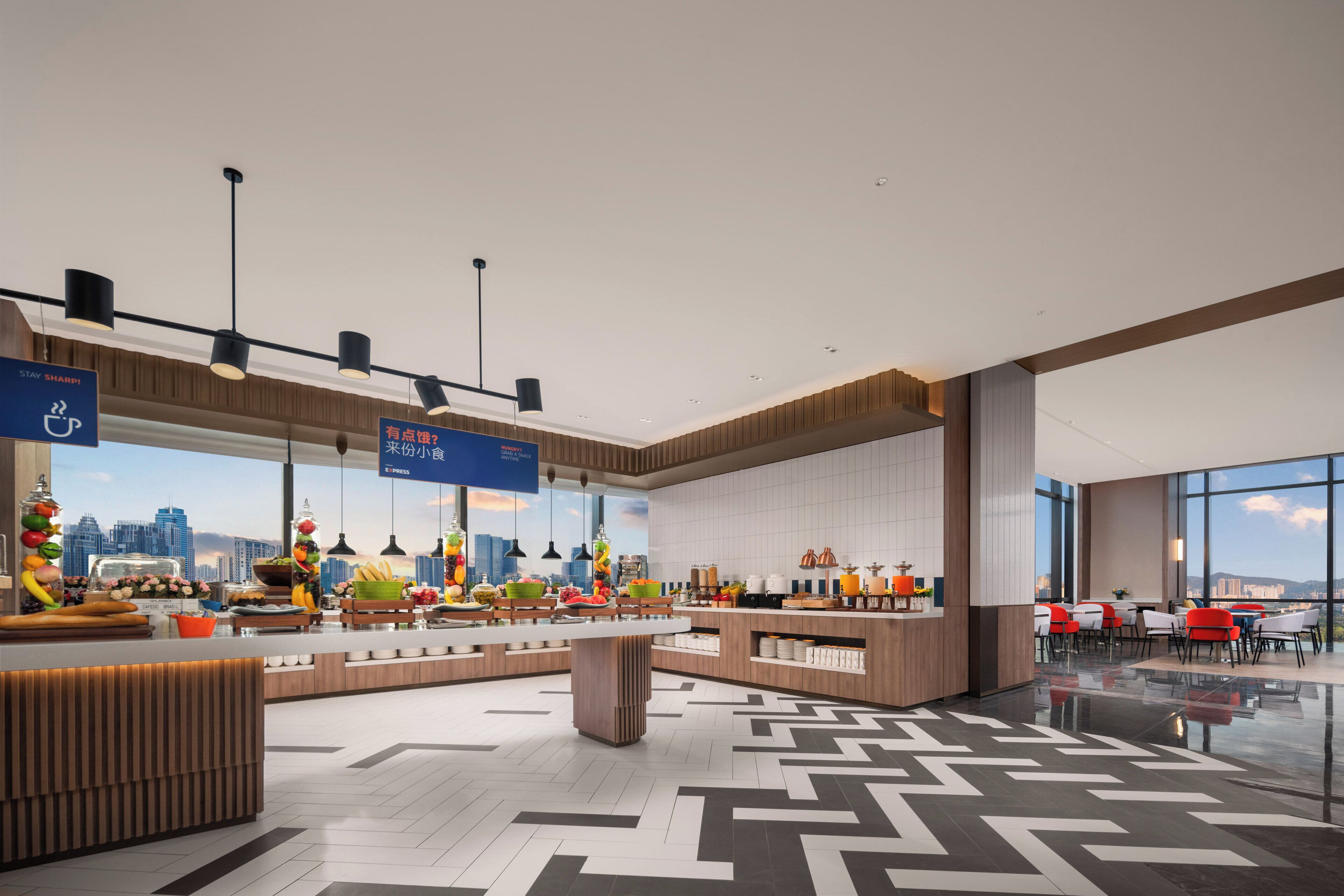 A modern hotel lobby with a central island, seating areas, and a city view.