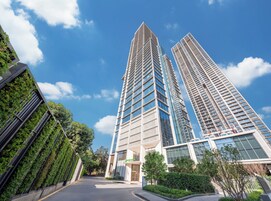 A modern building with a glass facade, surrounded by greenery and a clear blue sky.