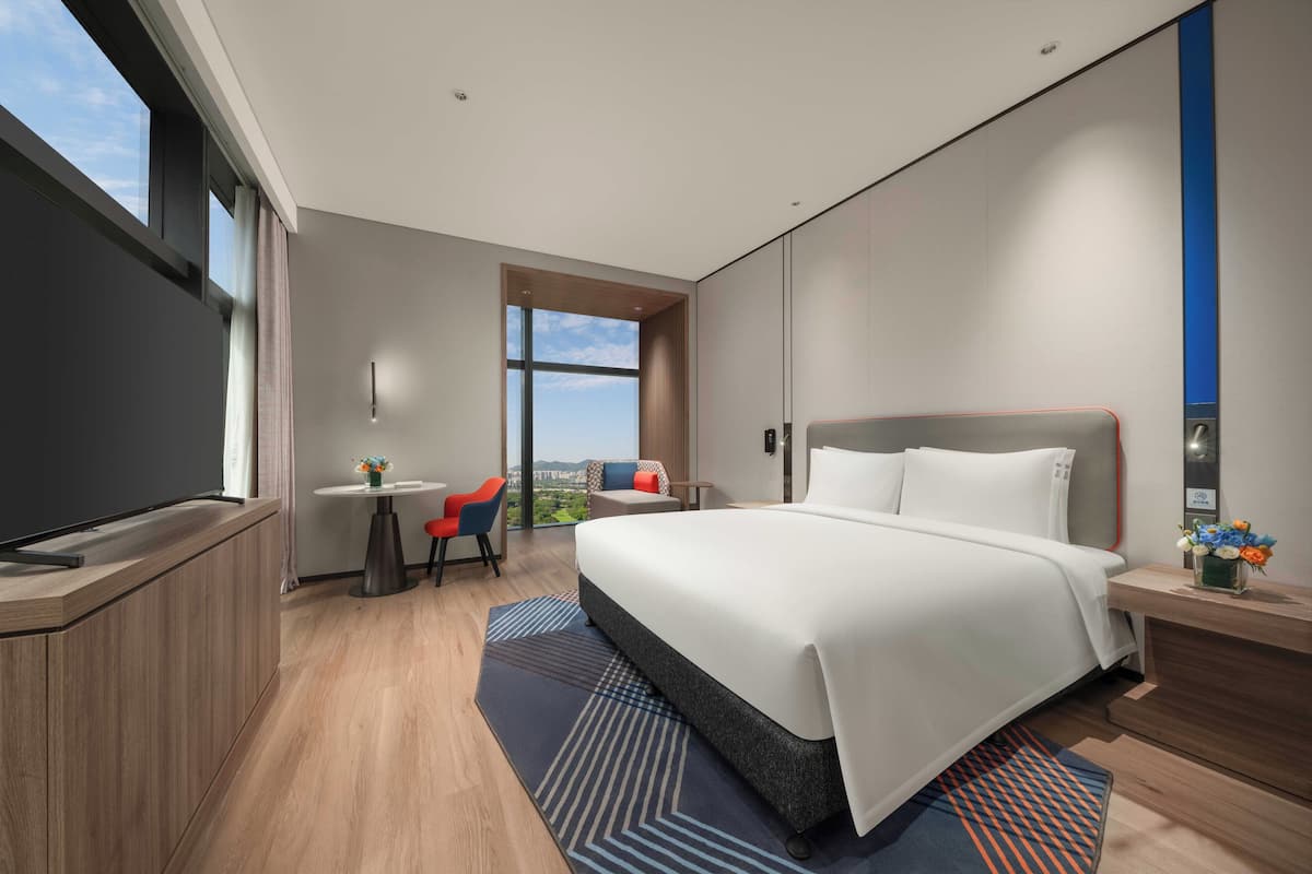 Una habitación de hotel moderna con una cama grande, un escritorio y vistas al exterior.