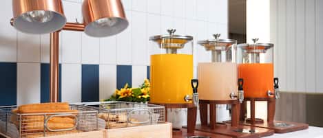 Un comptoir de cuisine aménagé en coin café, comprenant deux lampes en cuivre, un panier de fruits et un distributeur d’eau.