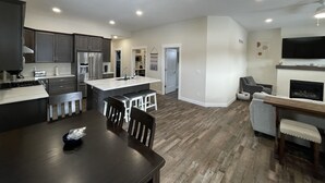 A modern kitchen with dark cabinets, a central island, and a dining area with a table and chairs. - New Construction Home, 1 block to Legendary Surf District/ Blocks to downtown (Clear Lake)